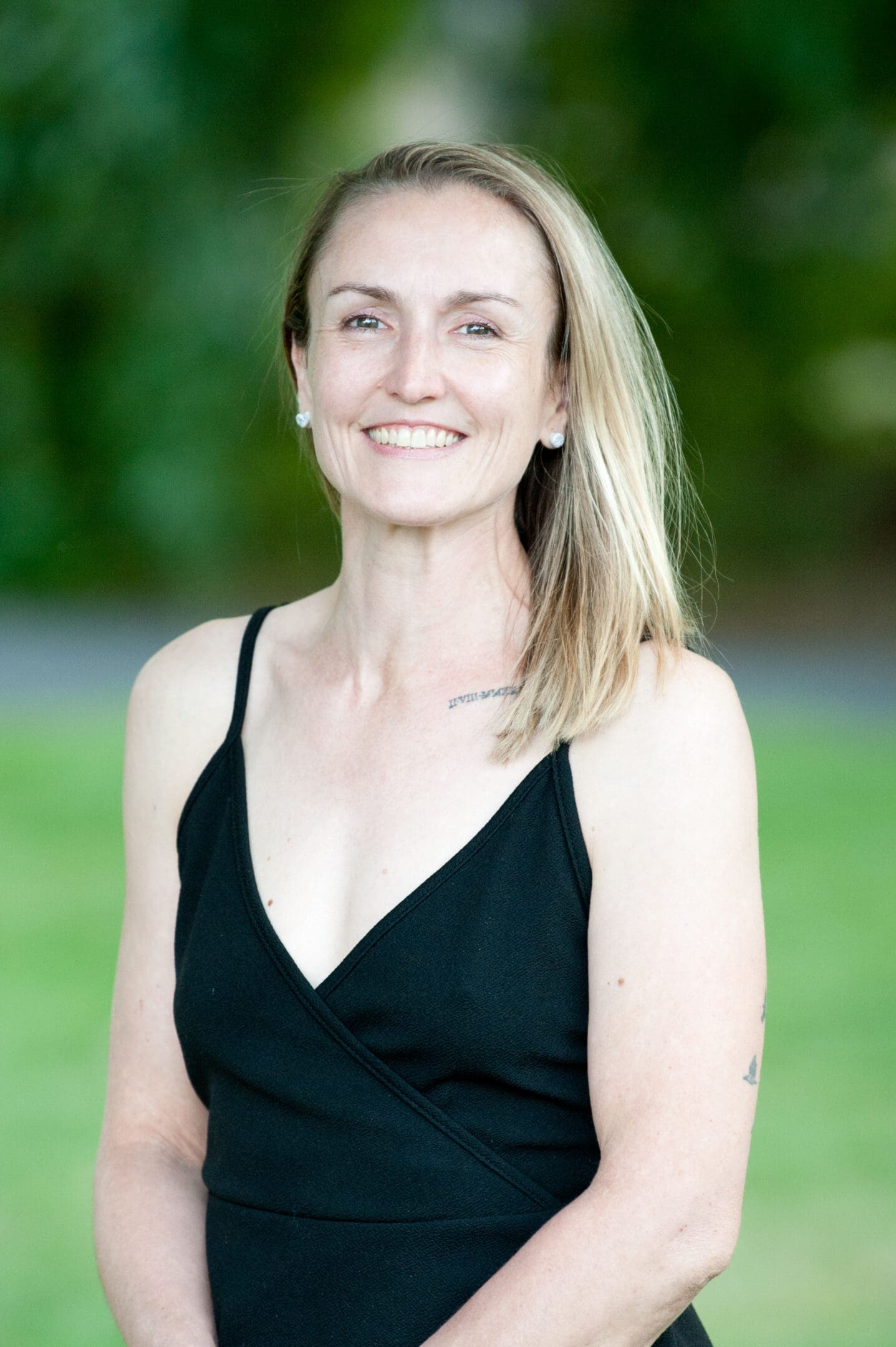 A smiling woman in a black dress outdoors.