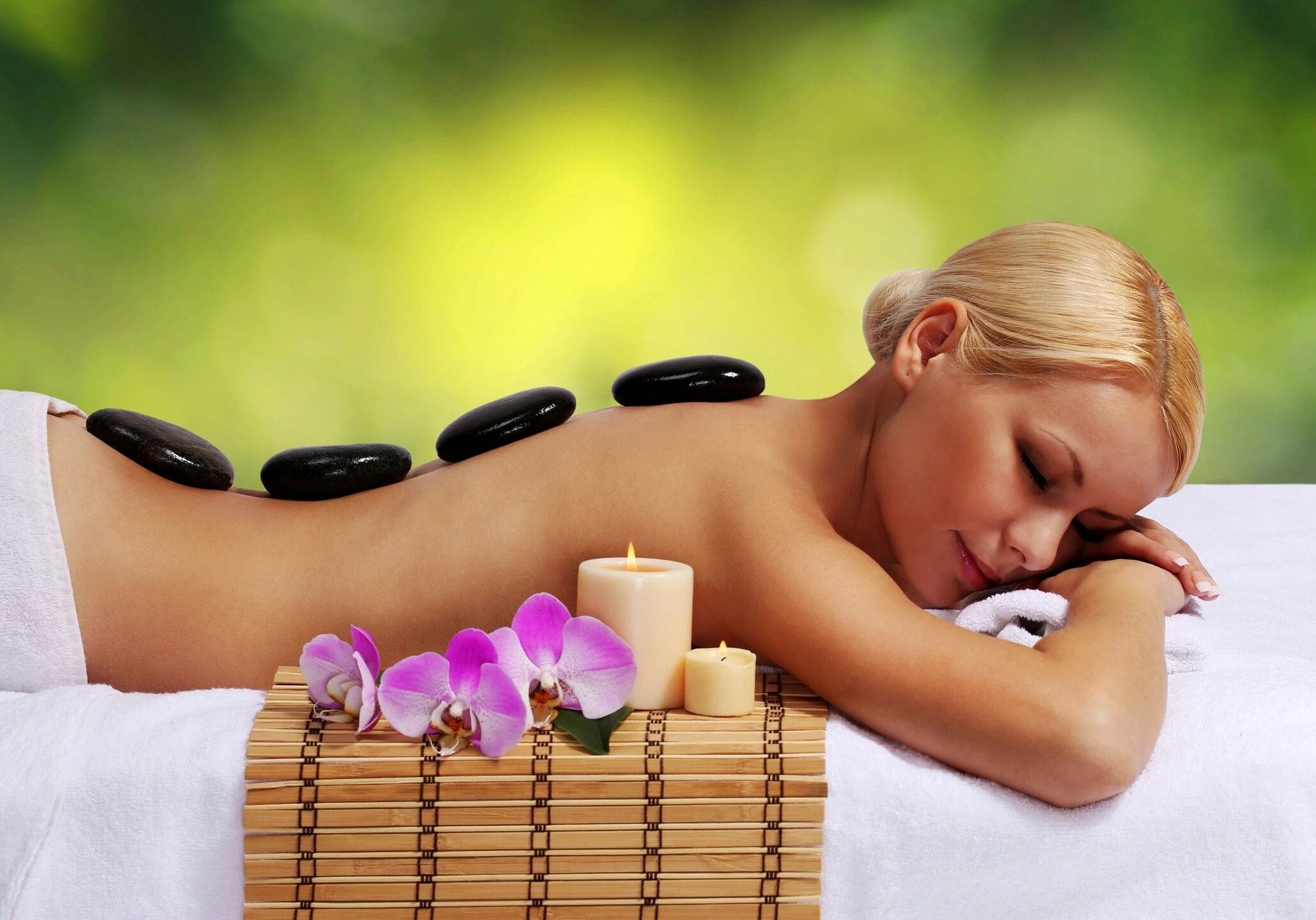 Woman enjoying a hot stone massage with orchid flowers nearby.